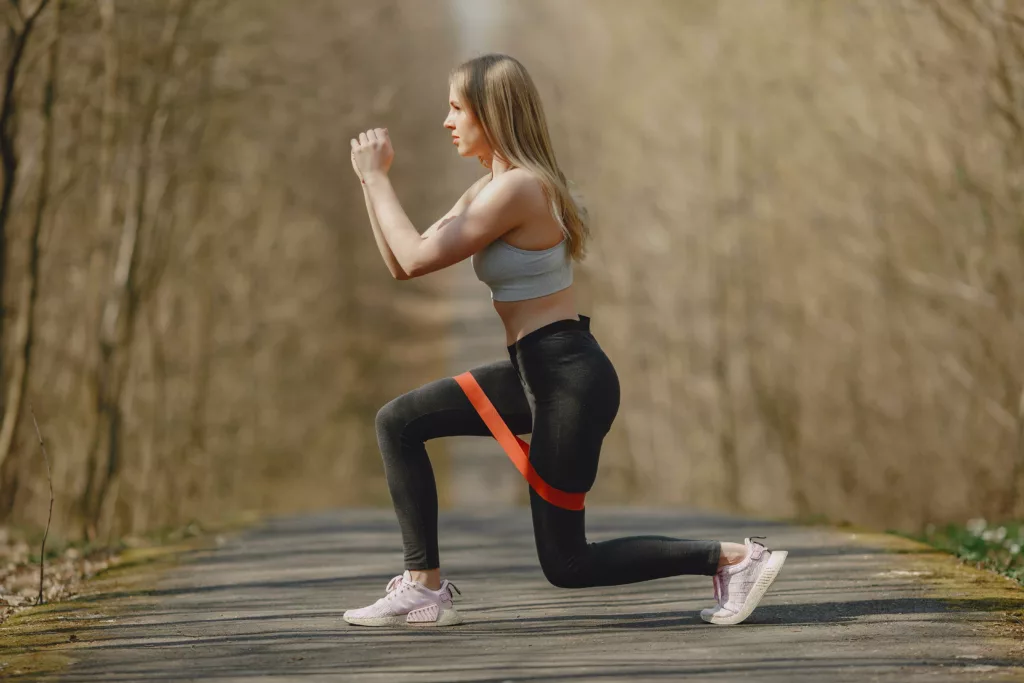 Donna che esegue esercizi di potenziamento muscolare con una fascia elastica rossa all'aperto